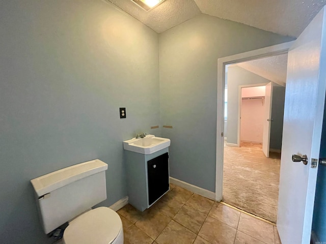 bathroom with a textured ceiling, vanity, tile patterned flooring, toilet, and lofted ceiling