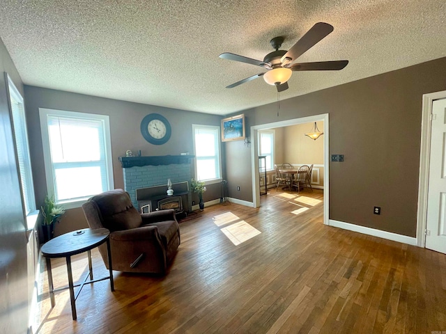 living room featuring a textured ceiling, a wood stove, a brick fireplace, ceiling fan, and hardwood / wood-style flooring