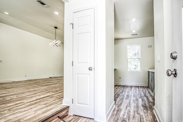 hallway with an inviting chandelier, wood finished floors, visible vents, and baseboards