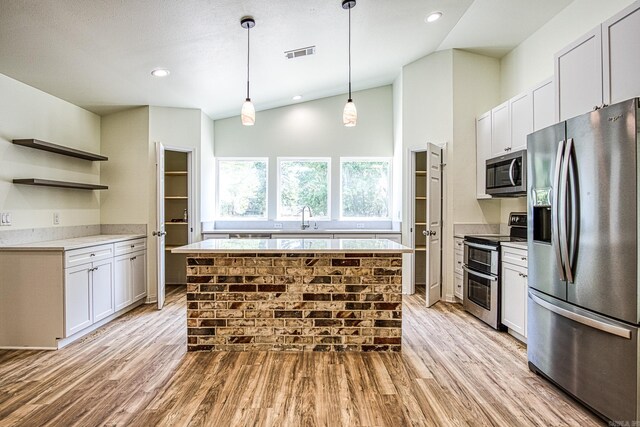 kitchen with light wood-type flooring, decorative light fixtures, appliances with stainless steel finishes, white cabinetry, and a kitchen island