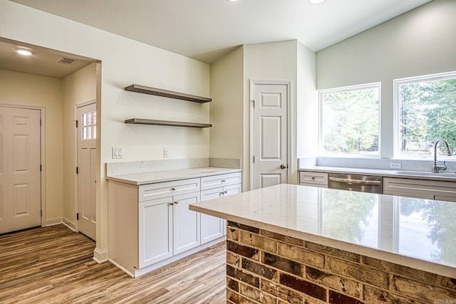 kitchen featuring light stone countertops, stainless steel dishwasher, sink, white cabinetry, and light wood-type flooring