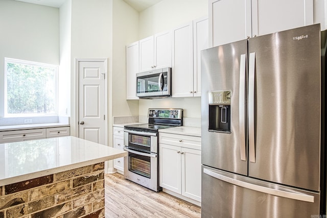 kitchen with appliances with stainless steel finishes, white cabinetry, light wood finished floors, and light stone countertops
