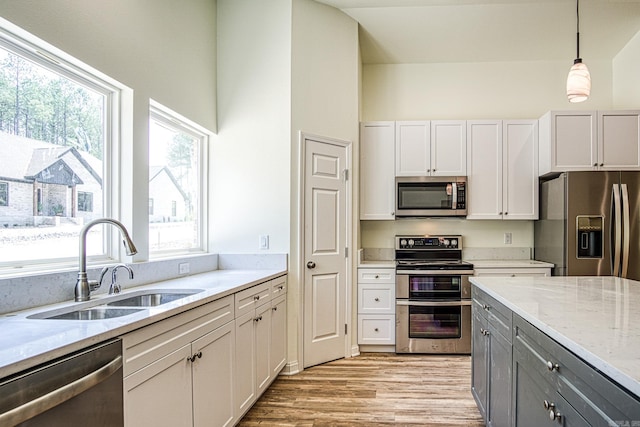 kitchen with hanging light fixtures, light wood-type flooring, light stone counters, stainless steel appliances, and sink