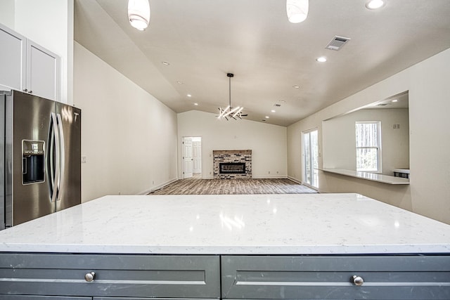 kitchen featuring visible vents, gray cabinetry, vaulted ceiling, light stone countertops, and stainless steel fridge with ice dispenser