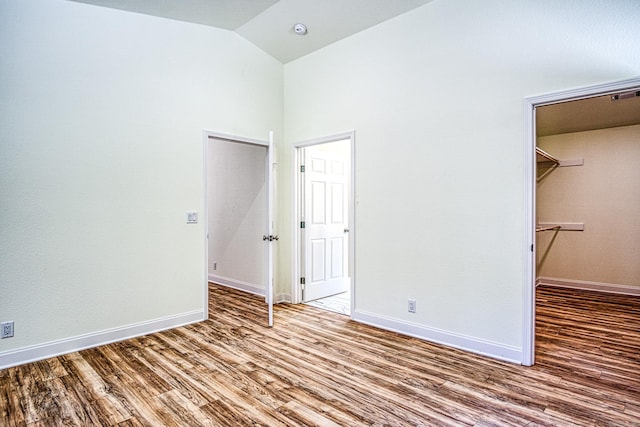 unfurnished bedroom with lofted ceiling, baseboards, a walk in closet, and wood finished floors