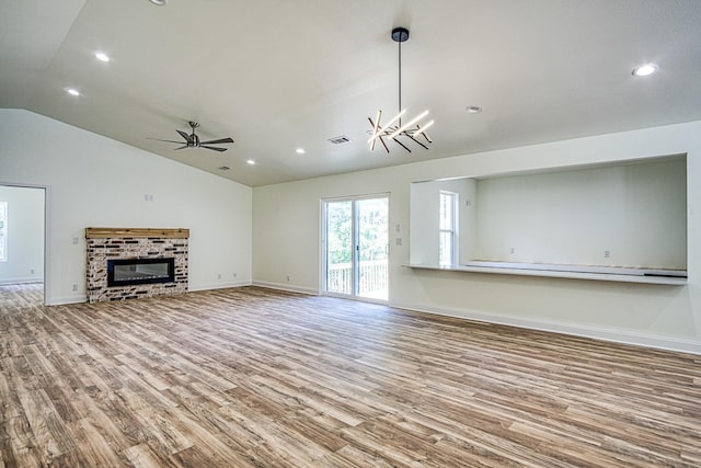unfurnished living room featuring a fireplace, lofted ceiling, visible vents, wood finished floors, and ceiling fan with notable chandelier