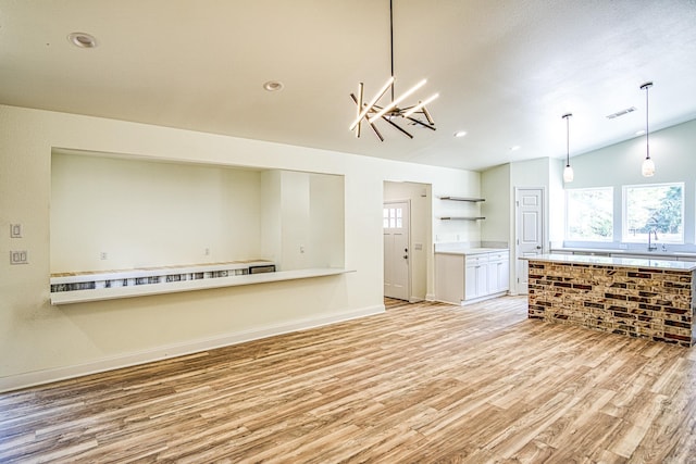 unfurnished living room with baseboards, visible vents, vaulted ceiling, light wood-style floors, and a sink