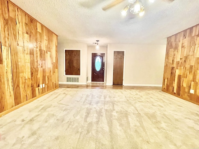 carpeted empty room with a ceiling fan, visible vents, wooden walls, and a textured ceiling