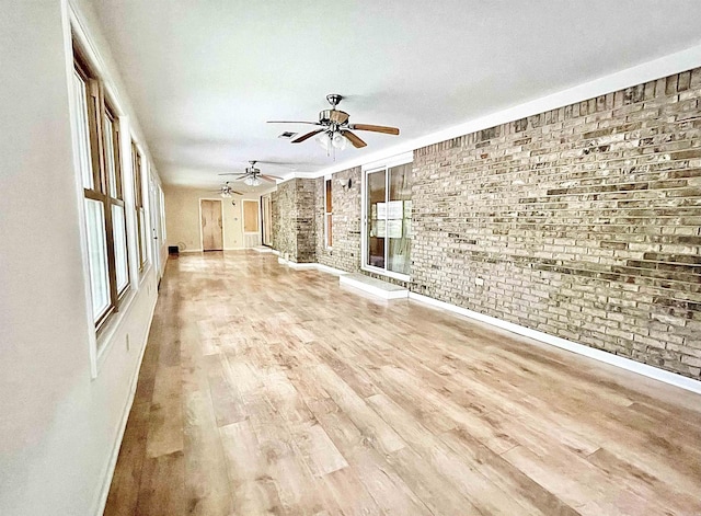 unfurnished living room with brick wall, wood finished floors, a ceiling fan, and baseboards