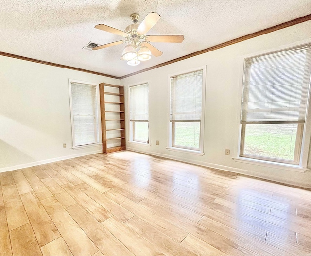 empty room featuring a textured ceiling, light wood-type flooring, a wealth of natural light, and crown molding