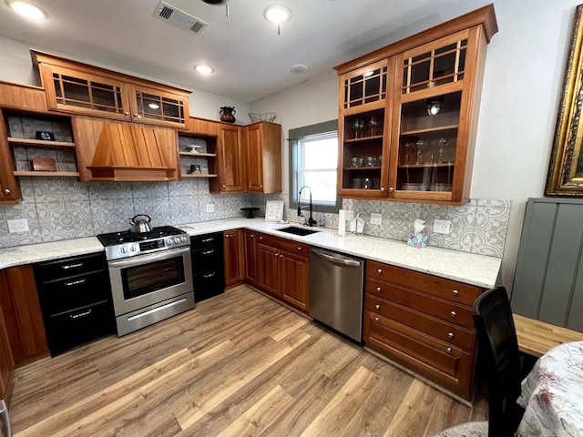 kitchen with tasteful backsplash, stainless steel appliances, sink, light stone countertops, and light hardwood / wood-style floors