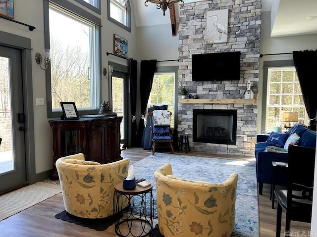 living room featuring high vaulted ceiling, plenty of natural light, wood-type flooring, and a stone fireplace