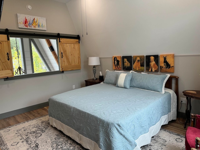 bedroom with a barn door, hardwood / wood-style floors, and lofted ceiling