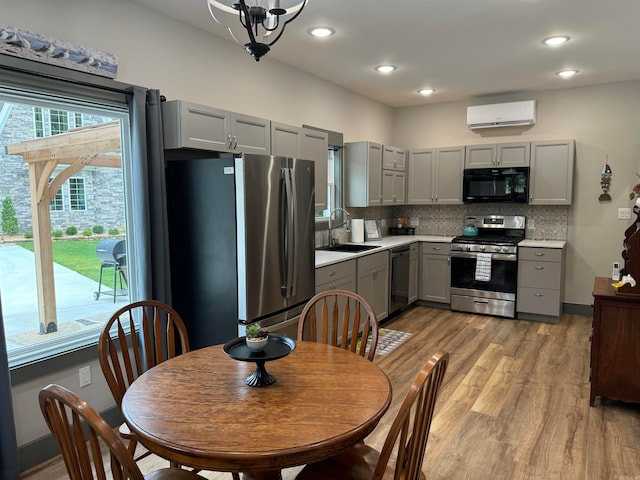 kitchen with an inviting chandelier, appliances with stainless steel finishes, a wall mounted air conditioner, light hardwood / wood-style floors, and sink