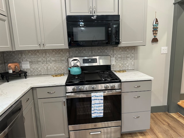 kitchen featuring gray cabinetry, light hardwood / wood-style flooring, tasteful backsplash, stainless steel appliances, and light stone counters