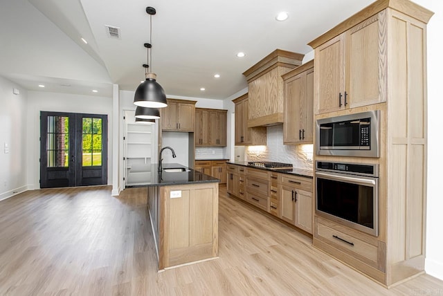 kitchen with light hardwood / wood-style flooring, appliances with stainless steel finishes, an island with sink, hanging light fixtures, and lofted ceiling