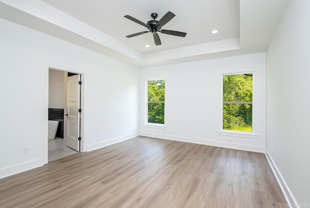 unfurnished bedroom featuring light wood-type flooring, a tray ceiling, and ceiling fan