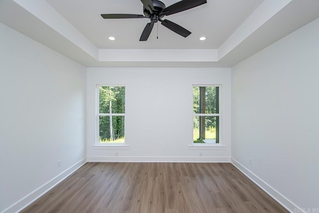 unfurnished room with a raised ceiling, wood-type flooring, ceiling fan, and a wealth of natural light