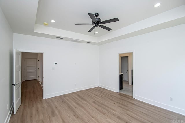 spare room with a tray ceiling, ceiling fan, and light hardwood / wood-style floors