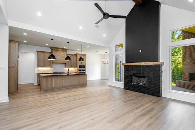 kitchen with ceiling fan with notable chandelier, light hardwood / wood-style floors, a kitchen island with sink, high vaulted ceiling, and decorative backsplash