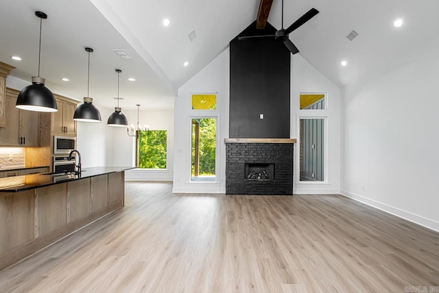 kitchen featuring stainless steel appliances, beamed ceiling, ceiling fan, a stone fireplace, and high vaulted ceiling