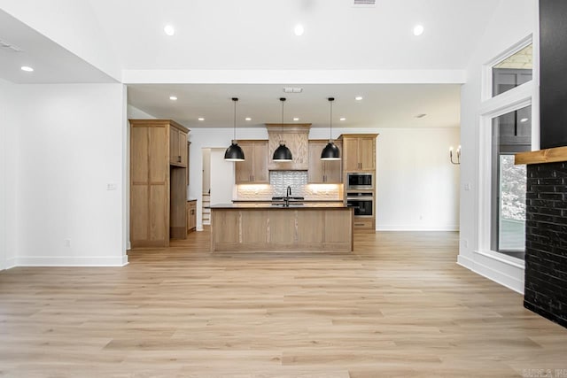 kitchen featuring light hardwood / wood-style flooring, decorative light fixtures, an island with sink, sink, and appliances with stainless steel finishes