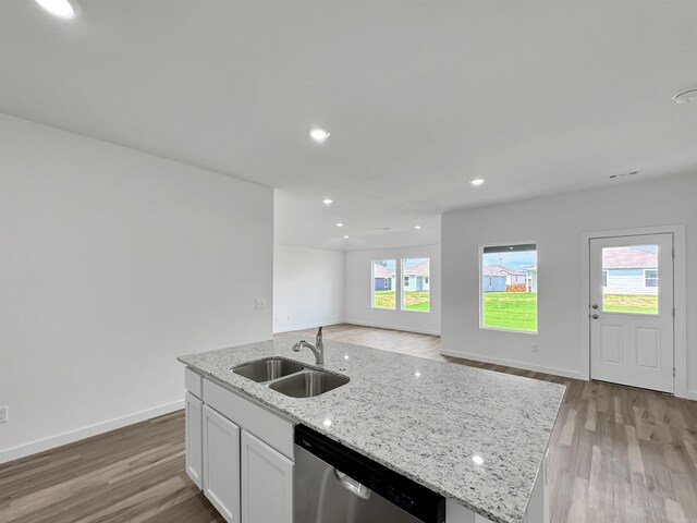 kitchen with light stone countertops, sink, stainless steel dishwasher, a kitchen island with sink, and white cabinets