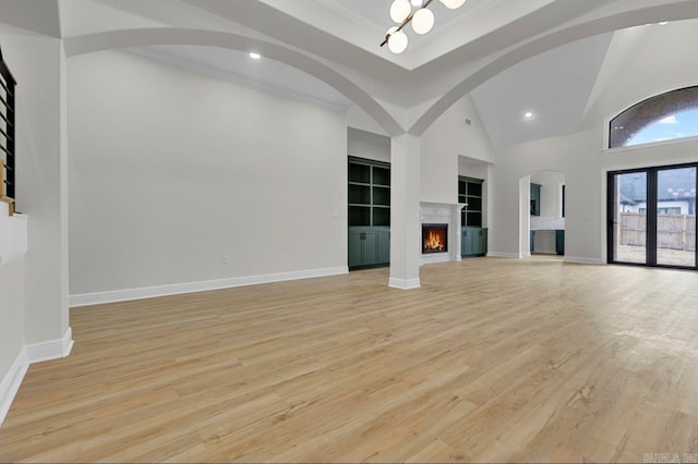 unfurnished living room featuring light wood-type flooring, built in shelves, high vaulted ceiling, and ornamental molding