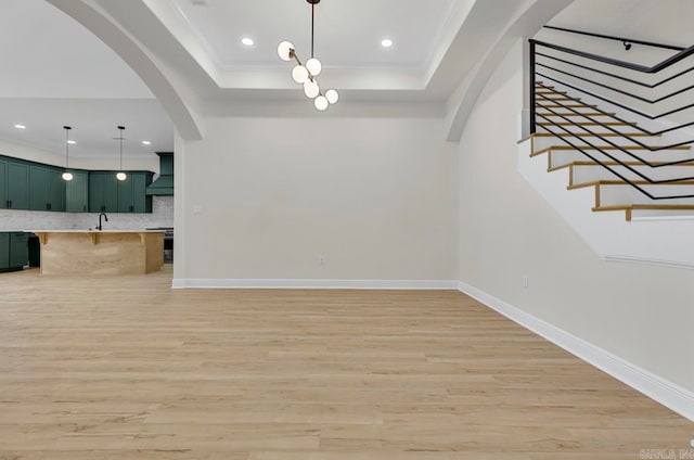 unfurnished living room with sink, a raised ceiling, light hardwood / wood-style floors, and ornamental molding