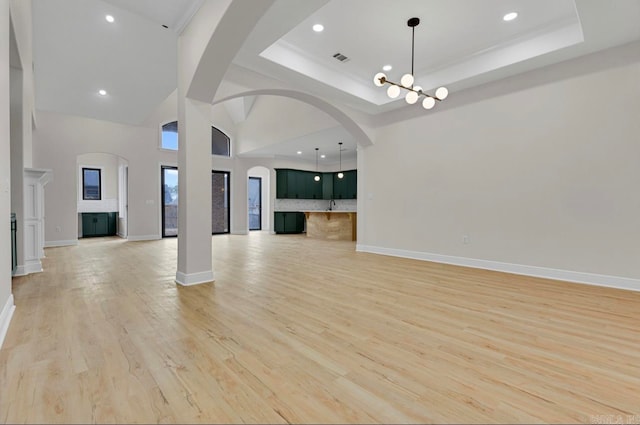 unfurnished living room with light wood-type flooring, high vaulted ceiling, a raised ceiling, and a notable chandelier