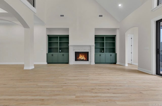 unfurnished living room featuring built in shelves, high vaulted ceiling, a premium fireplace, and light hardwood / wood-style flooring