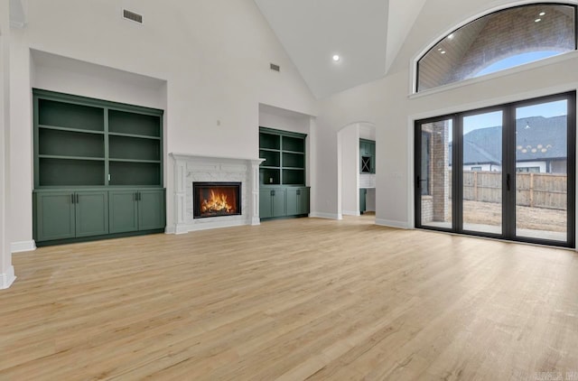 unfurnished living room with a high end fireplace, light wood-type flooring, high vaulted ceiling, and built in shelves