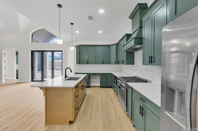 kitchen with light wood-type flooring, backsplash, sink, appliances with stainless steel finishes, and a center island with sink