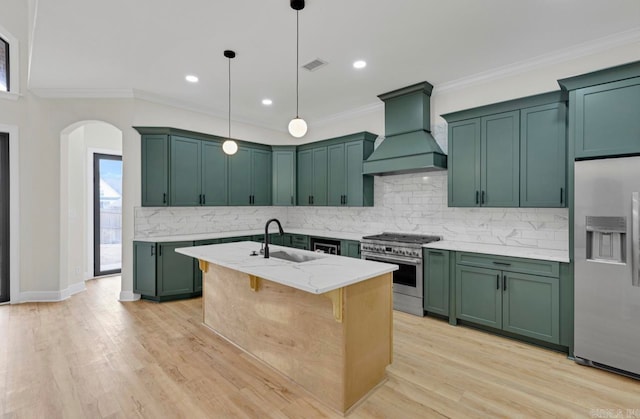 kitchen with backsplash, custom range hood, appliances with stainless steel finishes, sink, and a center island with sink