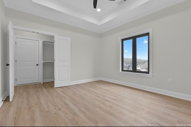 unfurnished bedroom featuring a closet, ceiling fan, a tray ceiling, and light hardwood / wood-style floors