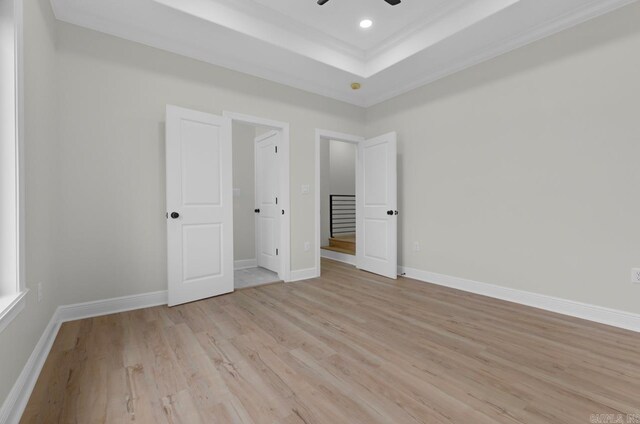 unfurnished bedroom featuring light wood-type flooring, a tray ceiling, ceiling fan, and crown molding