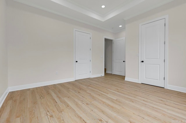 spare room with a tray ceiling, light hardwood / wood-style floors, and ornamental molding