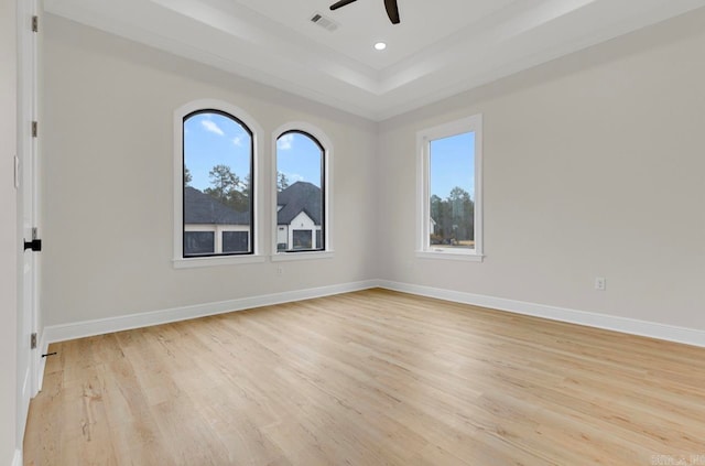 empty room featuring light wood-type flooring, a tray ceiling, and ceiling fan