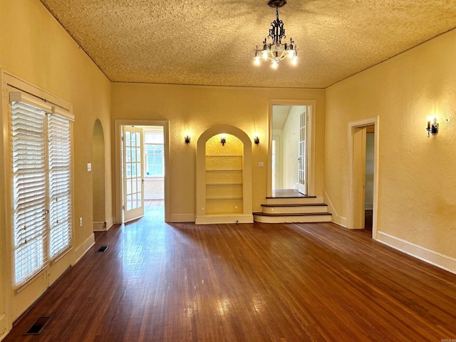 unfurnished living room with a textured ceiling, dark hardwood / wood-style floors, a chandelier, and built in features