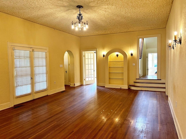 empty room featuring dark wood-type flooring, a textured ceiling, a healthy amount of sunlight, and built in shelves