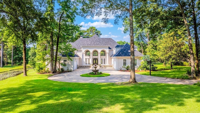 view of front of property featuring driveway, french doors, roof with shingles, stucco siding, and a front lawn