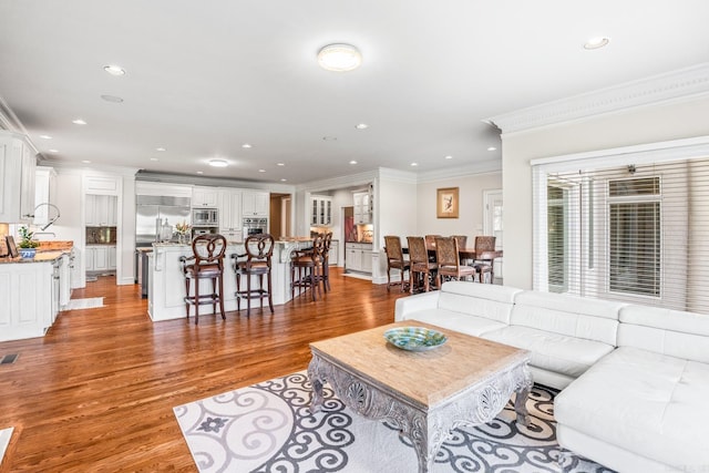 living room featuring crown molding, visible vents, wood finished floors, and recessed lighting