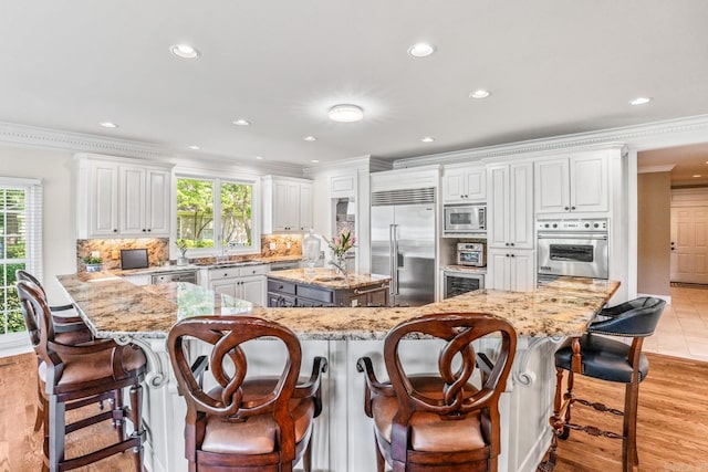 kitchen with a breakfast bar, crown molding, backsplash, a kitchen island, and built in appliances