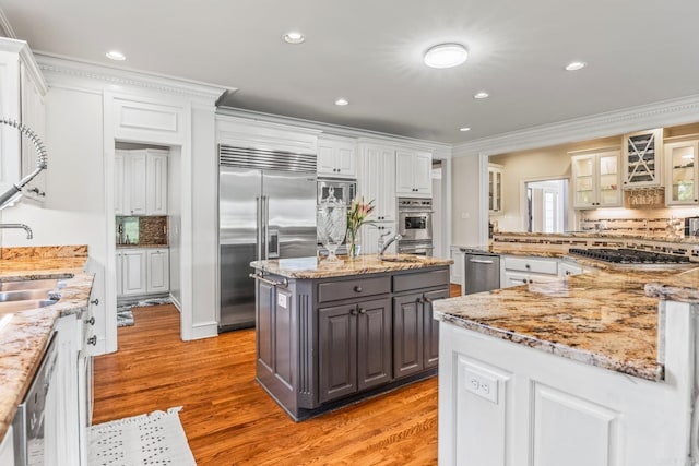 kitchen with a center island, crown molding, light wood-style flooring, glass insert cabinets, and built in appliances