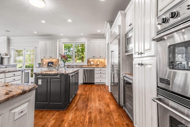 kitchen featuring decorative backsplash, ornamental molding, white cabinetry, built in appliances, and beverage cooler