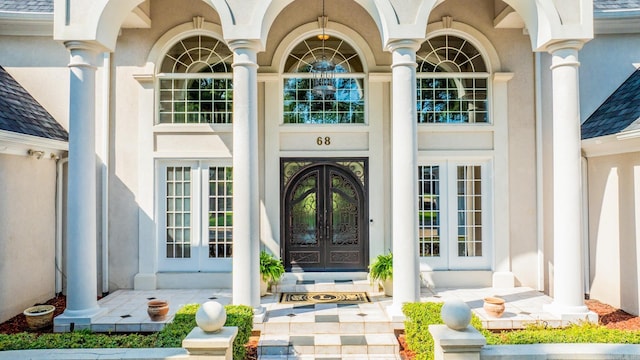 entrance to property with french doors, a shingled roof, and stucco siding