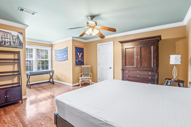 bedroom with baseboards, visible vents, crown molding, and wood finished floors