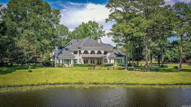 back of property featuring a water view, a chimney, and a lawn