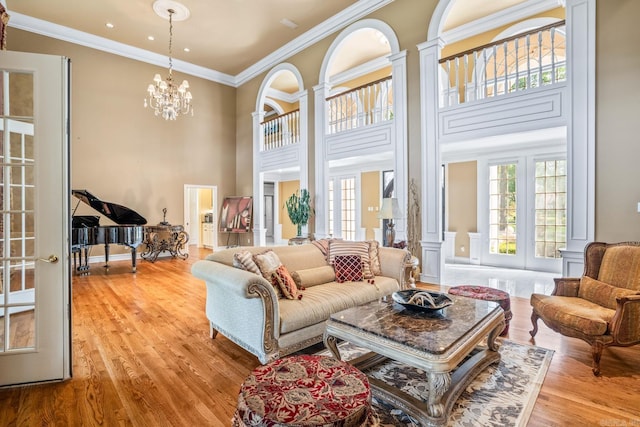 living area with ornamental molding, a high ceiling, french doors, light wood-type flooring, and a notable chandelier