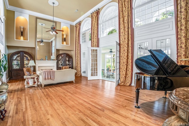 living area with french doors, a fireplace, a towering ceiling, ornamental molding, and wood finished floors